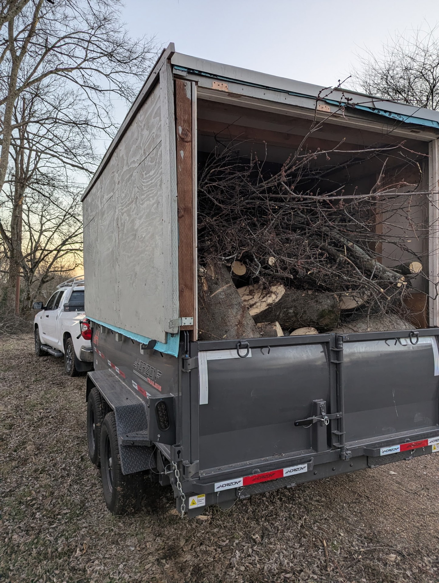 Hauling Patriots Horizon dump trailer with extended sidewalls fully loaded with tree limbs, branches, and cut log sections after a Nashville-area storm cleanup job